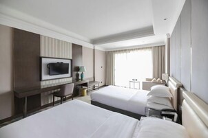 Habitación de hotel con dos camas, un escritorio, un televisor y una ventana con cortinas.