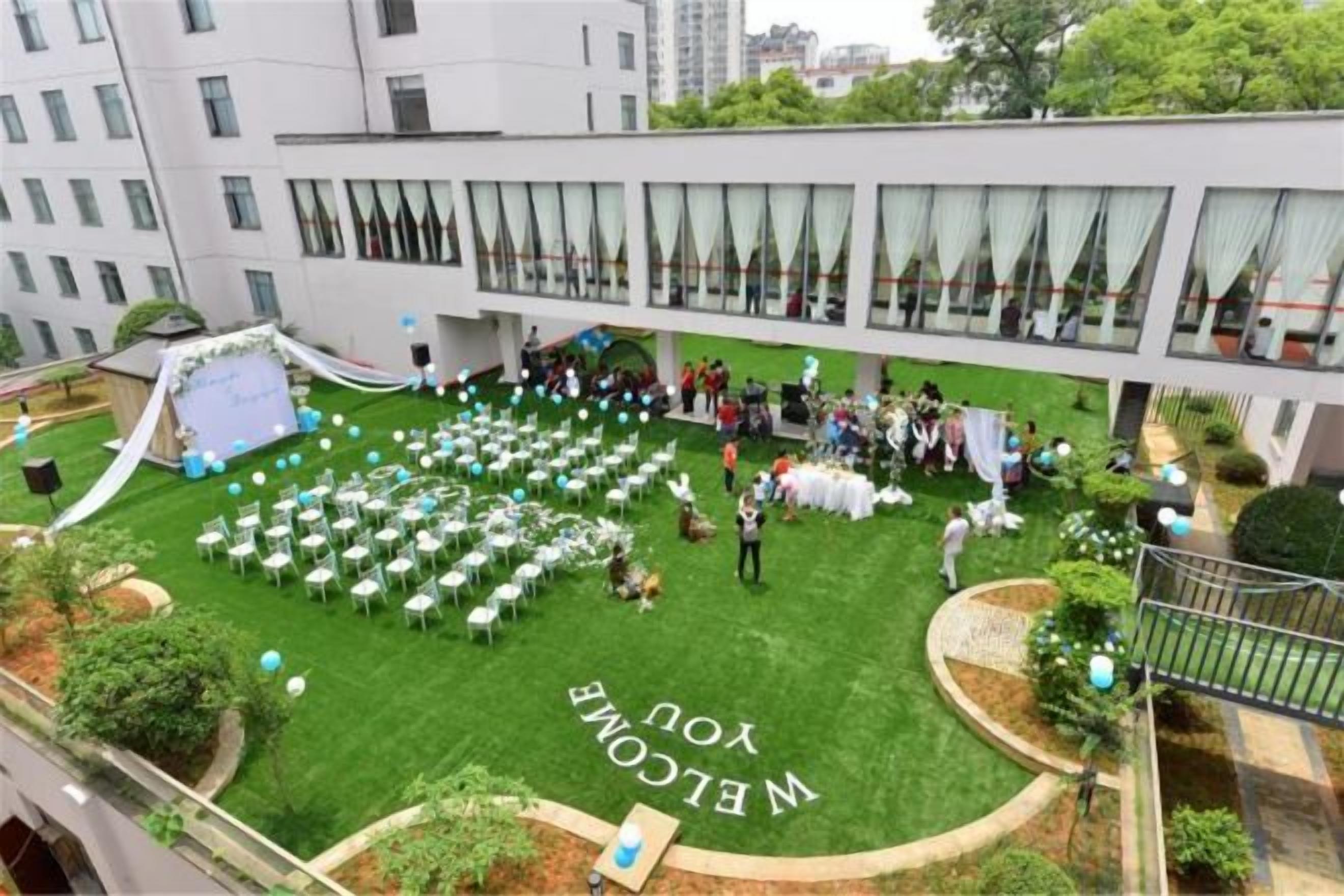 An outdoor event space with tables and chairs arranged for an event, surrounded by a building with large windows.