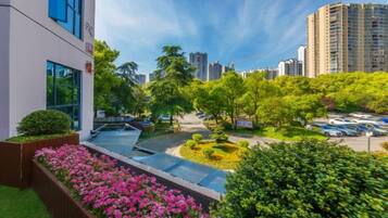 A modern building with a rooftop garden, surrounded by greenery and high-rise buildings.