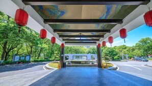 A covered walkway with red lanterns, a tiled floor, and a view of a park with trees and a fountain. - Baoqing Villa (Shaoyang)