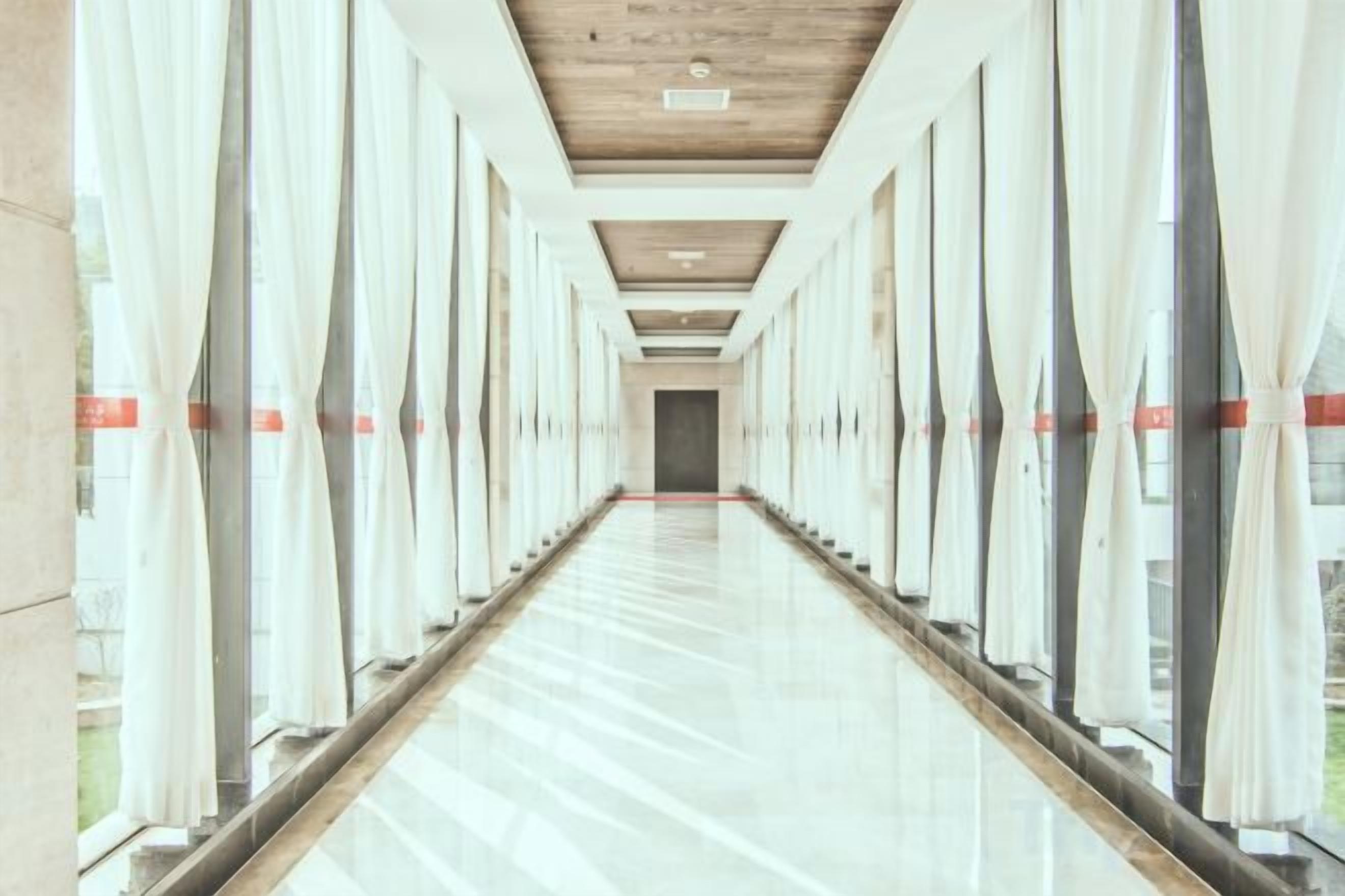 A long, narrow hallway with large windows on both sides, leading to a door at the end.
