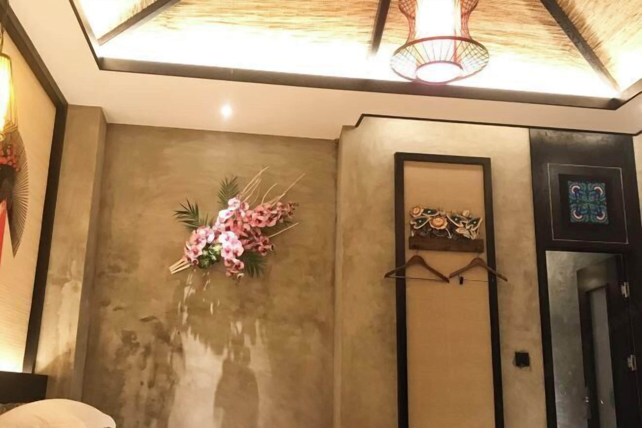 A room with a large mirror, a wall-mounted shelf with decorative items, and a ceiling light fixture.