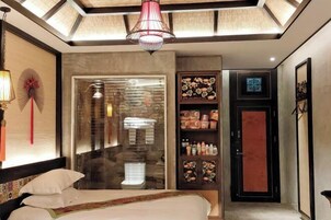 Habitación de hotel con una cama, un vidrio que da al baño, un minibar y una puerta roja.