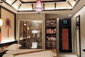 A hotel room with a bed, a glass door leading to a bathroom, a minibar, and a red door. - Yixunli Theme Hotel (Luoping)