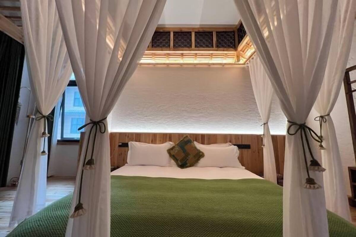 Ein Schlafzimmer mit einem Bett, weißen Vorhängen und einer grünen Decke.