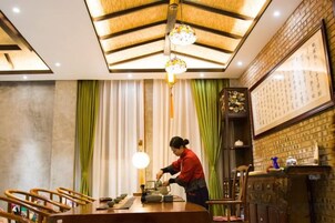 Interior de restaurante con techo de madera, cortinas verdes y una persona preparando comida en la barra.