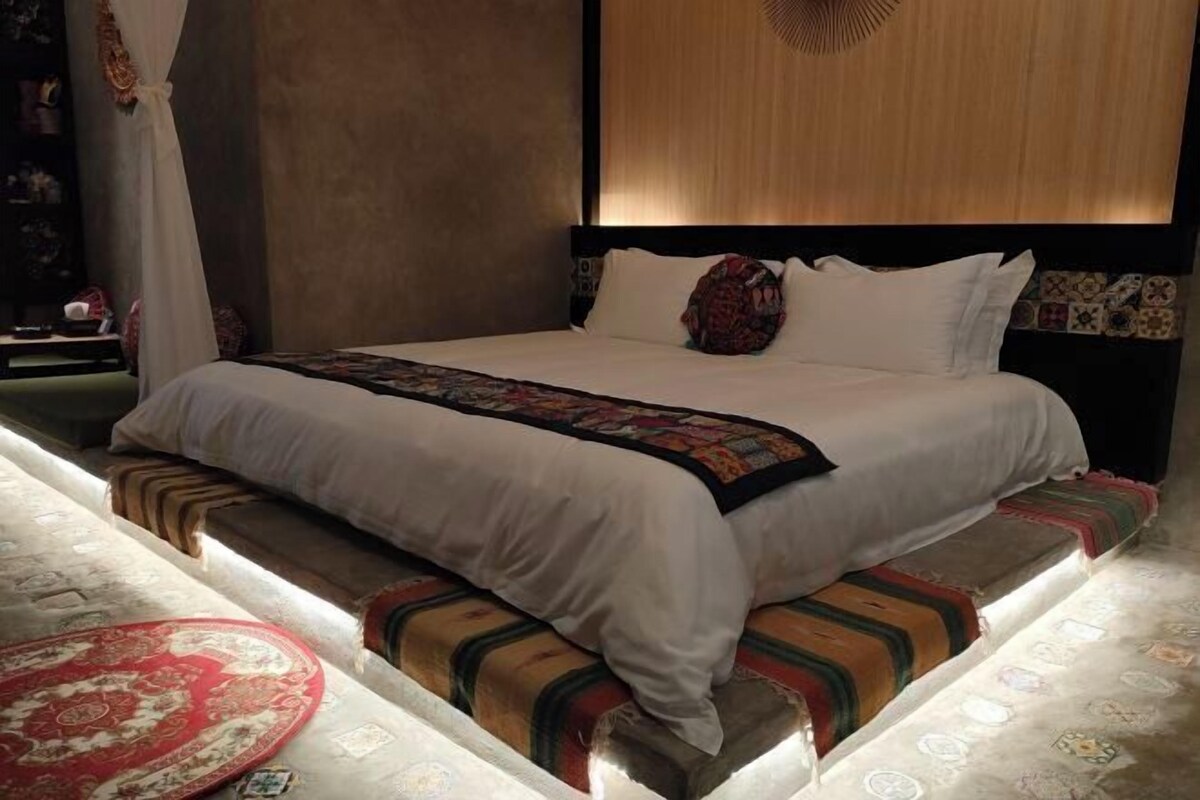 Una cama con edredón blanco, una colcha estampada y un cabecero con panel de madera.