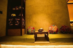 A room with a low table, cushions, and a shelf with decorative items. - Yixunli Theme Hotel (Luoping)