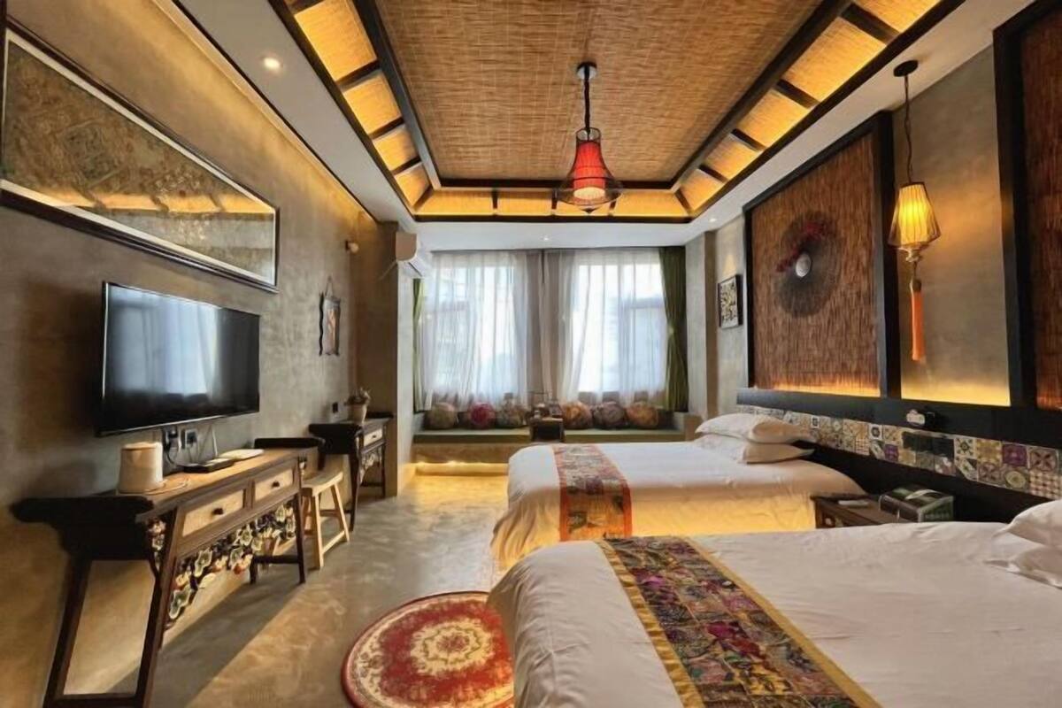 Ein Hotelzimmer mit großem Flachbildfernseher, zwei Betten, einer Schlafcouch, einem Holztischempfangstresen und einem großen Fenster mit Vorhängen.