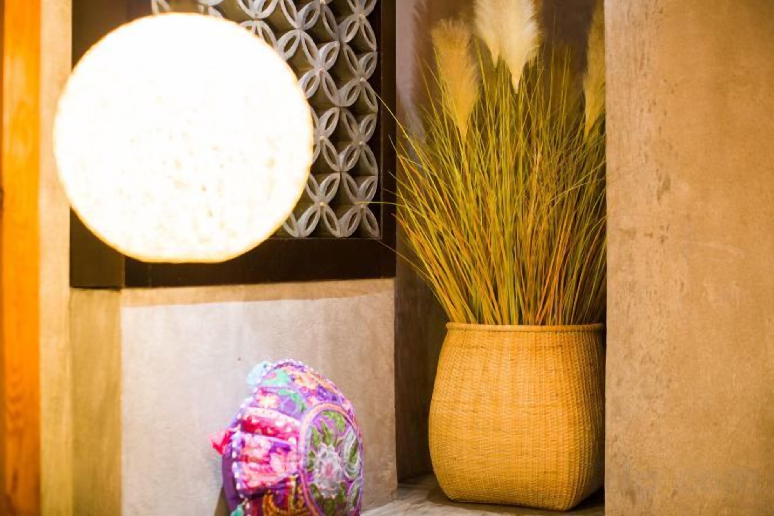 A room with a hanging light fixture, a woven basket with tall grass, and a patterned wall.
