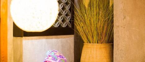 A room with a hanging light fixture, a woven basket with tall grass, and a patterned wall.