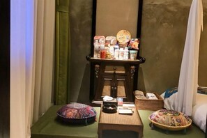 Una habitación con una pequeña mesa que exhibe varios objetos, una cama con dosel blanco y una pared con textura decorativa.