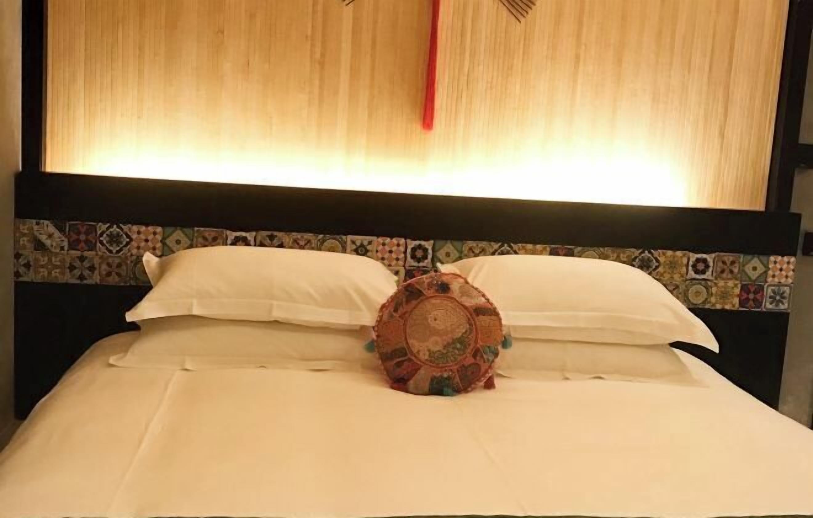 Un lit avec du linge de lit blanc, un coussin à motifs et une tête de lit ornée d’un motif géométrique.