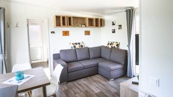 Ein modernes Wohnzimmer mit einem grauen Ecksofa, einem Holzschrank darüber und einem Essbereich mit Tisch und Stühlen.