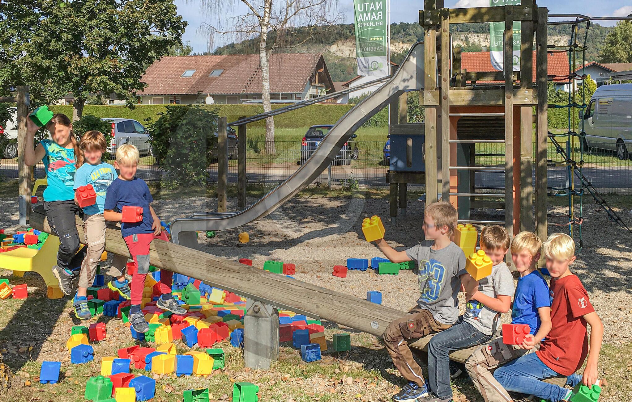 Kinder spielen mit Bauklötzen in der Nähe einer Spielgeräte-Anlage.