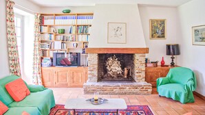 A living room with a fireplace, a bookshelf, a television, and two green armchairs. - Cozy home in Janailhac with outdoor swimming pool (Janailhac)