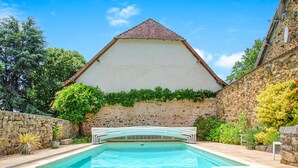 A swimming pool with a stone wall and a building with a tiled roof in the background. - Cozy home in Janailhac with outdoor swimming pool (Janailhac)