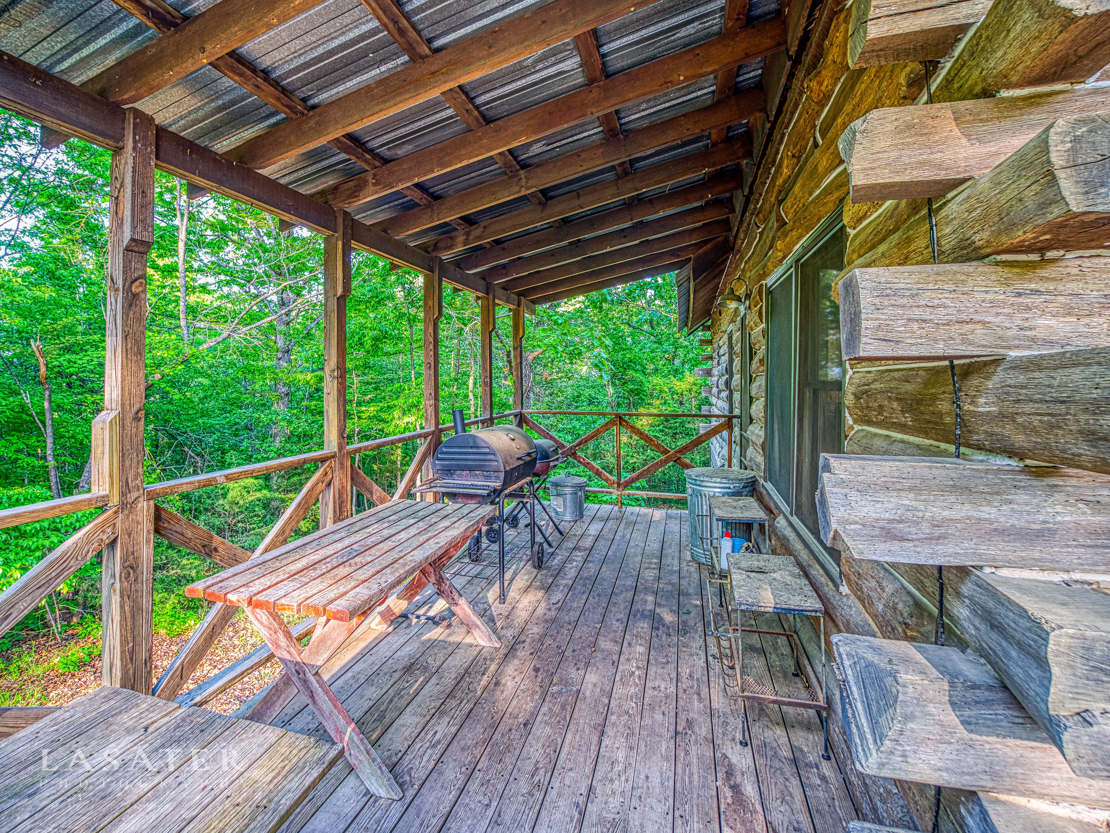 A wooden deck with a grill, a table, and a stone wall.