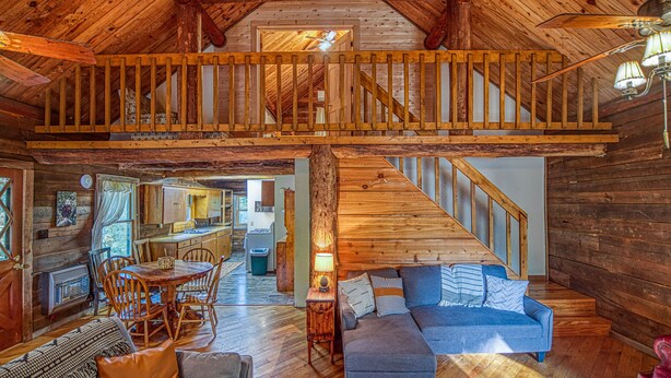 A spacious loft with a wooden staircase, a dining area, and a cozy seating area with a sofa and ottoman.