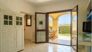 Ein Zimmer mit einer Glasschiebetür, die auf eine Außenpatio mit Tisch und Stühlen führt, einem weißen Schrank mit Schubladen und einem Fernseher auf einem Standfuß.