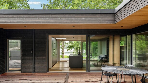 A modern house with a wooden deck, a glass door leading to a kitchen, and a view of a lake. - Gorgeous home in Bryrup with kitchen (Bryrup)