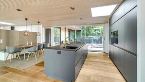 A modern kitchen with a central island, wooden ceiling, and large windows. - Gorgeous home in Bryrup with kitchen (Bryrup)