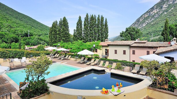 Un espace piscine doté de chaises longues et de parasols, entouré de verdure et de bâtiments.