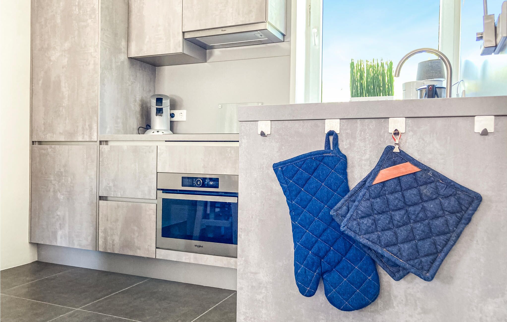 Una cucina moderna con forno a incasso, macchina da caffè e una finestra con vista su piante verdi.