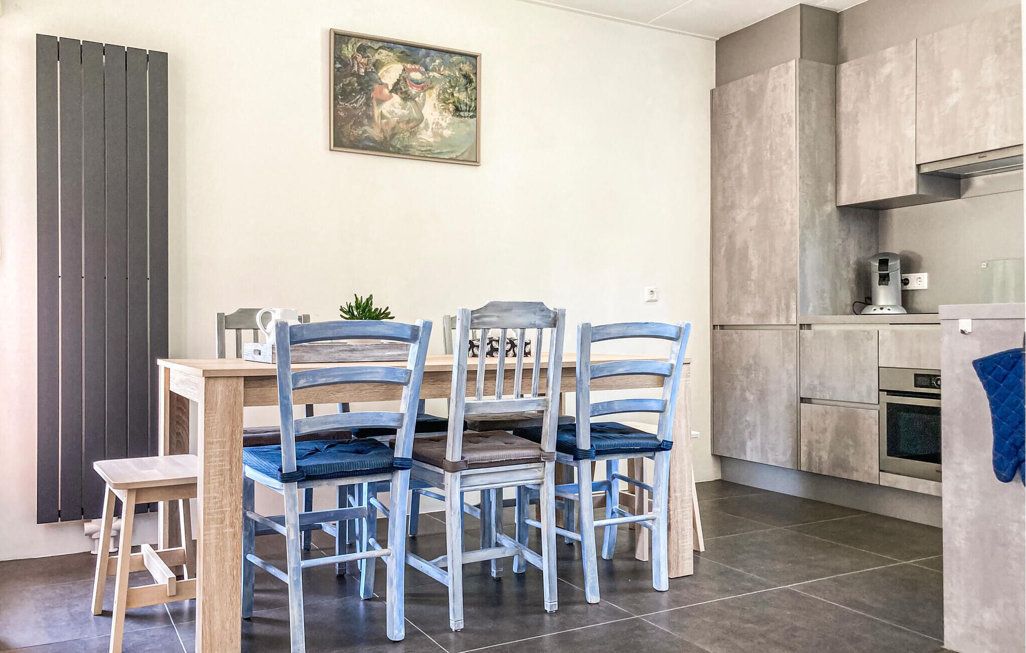 A modern kitchen with a dining area, featuring a wooden table, four chairs, and a painting on the wall.
