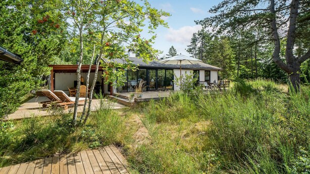 Un patio exterior moderno con terraza de madera, sillones de descanso y una zona de estar cubierta con mesa y sillas.