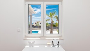 A room with a large window overlooking a swimming pool and palm trees, a white table with a butterfly sculpture, and a small round mirror. - Beautiful home in Trogir (Trogir)