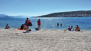 A pebbled beach with people sunbathing and swimming. - Beautiful home in Trogir (Trogir)