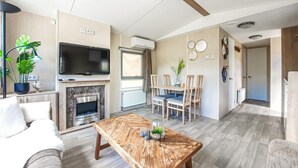 Ein modernes Wohnzimmer mit Flachbildfernseher, Kamin und Essbereich mit Holzsesseln und Tisch.