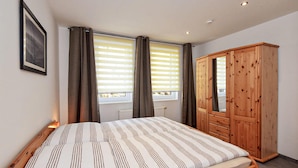 Une chambre à coucher avec un lit, une armoire en bois et une fenêtre avec des stores.