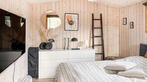 A bedroom with a wooden wall, a white dresser, a bed with patterned bedding, a mirror, and a ladder. - 3 bedroom cozy home in Skjern (Skjern)