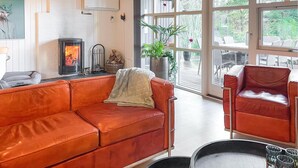 A living room with a red leather sofa, a red armchair, a fireplace, a large window, and a potted plant. - 3 bedroom cozy home in Skjern (Skjern)