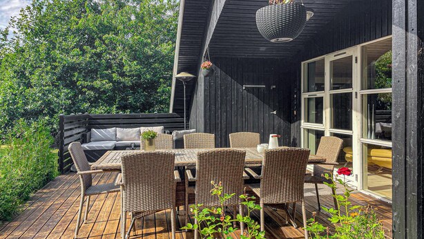 An outdoor patio with wicker furniture, a wooden deck, and a large window. - 3 bedroom cozy home in Skjern (Skjern)