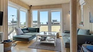 A modern living room with large windows, a sofa, a coffee table, and a TV.