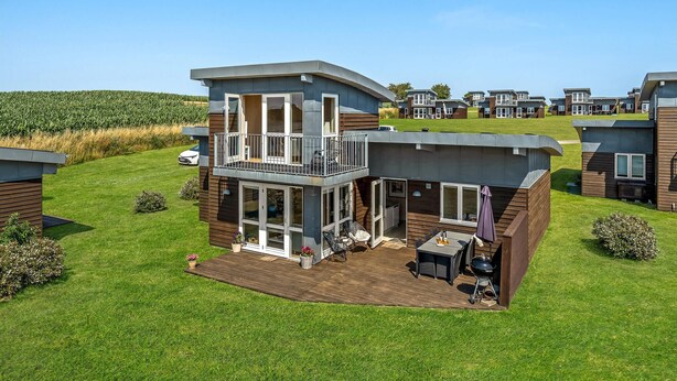 A modern two-story house with a balcony, a deck, and a barbecue area.