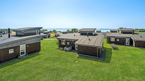 A row of modern, single-story cabins with flat roofs, arranged on a grassy area with a view of a body of water in the background.