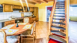 A kitchen with wooden cabinets, a dining table with chairs, and a red cushioned staircase. - Awesome home in Kamionki Male (Kamionki Male)