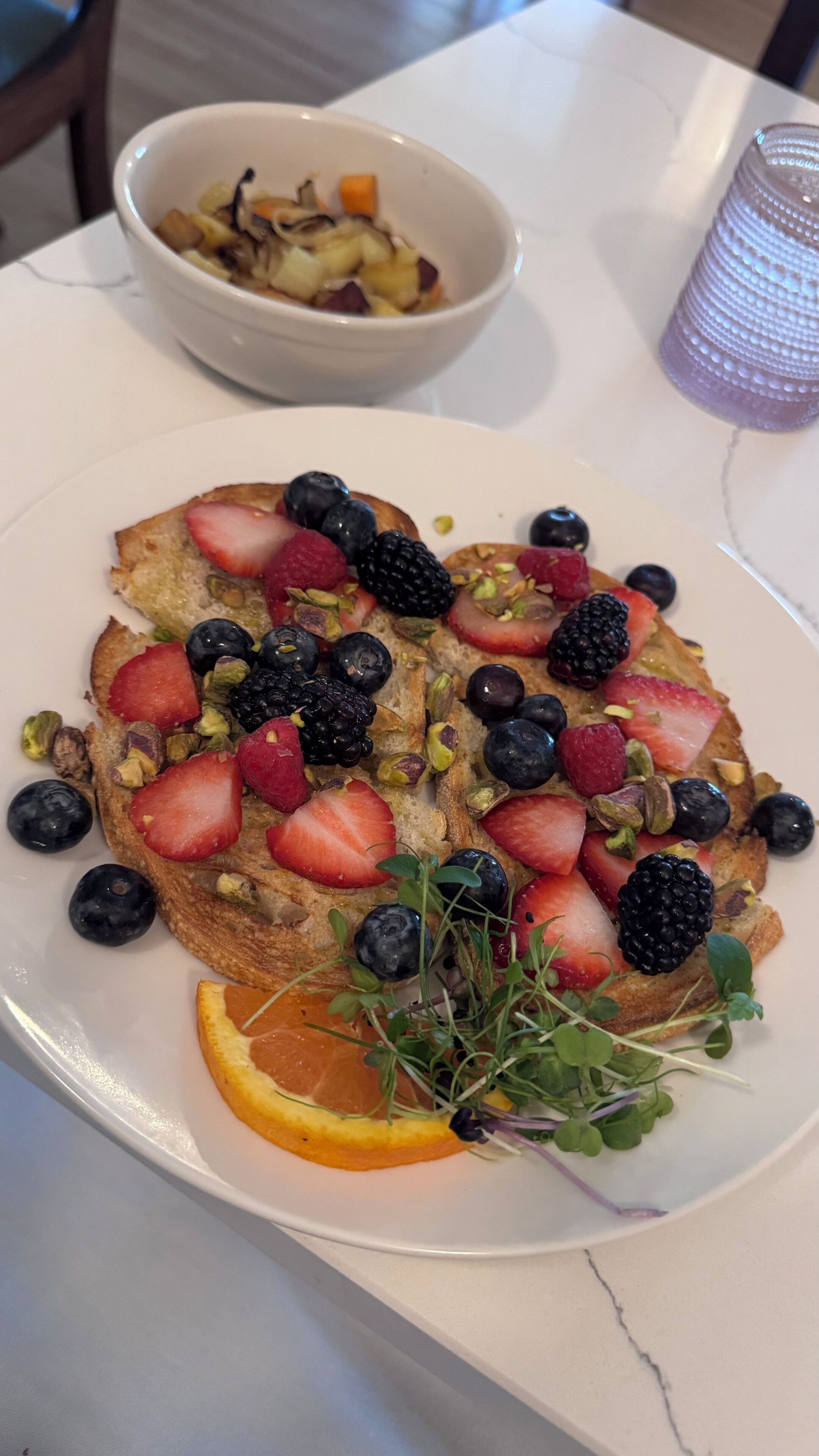 A plate of toast with fruit and nuts, a bowl of fruit salad, and a glass of water on a table.