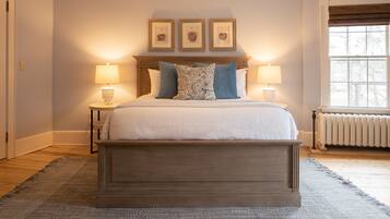 A bedroom with a large bed, two bedside lamps, a headboard with three framed pictures, and a window with a view of trees.