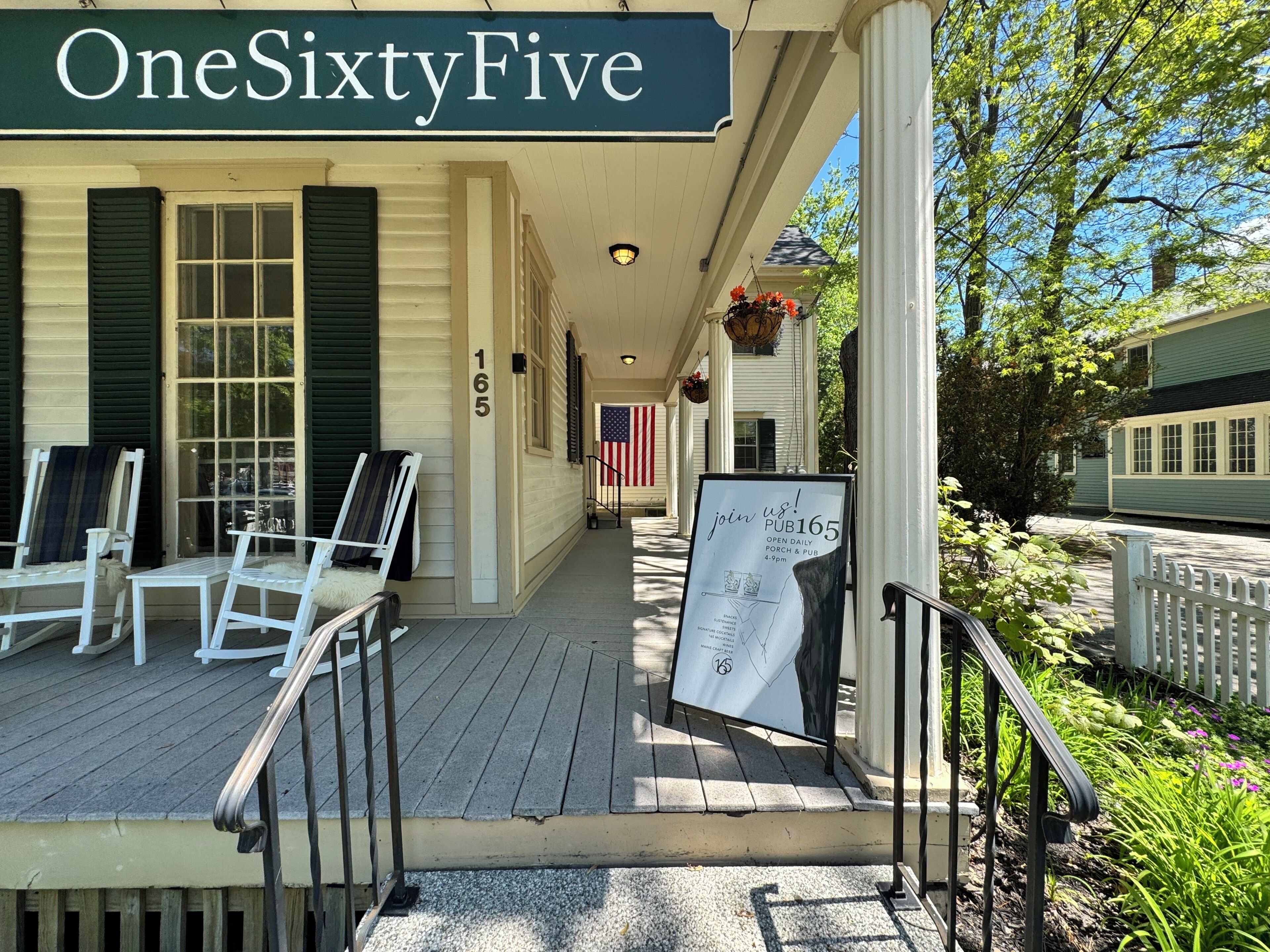 A porch with outdoor seating, a sign for PUB165, and a view of a building with a green facade.