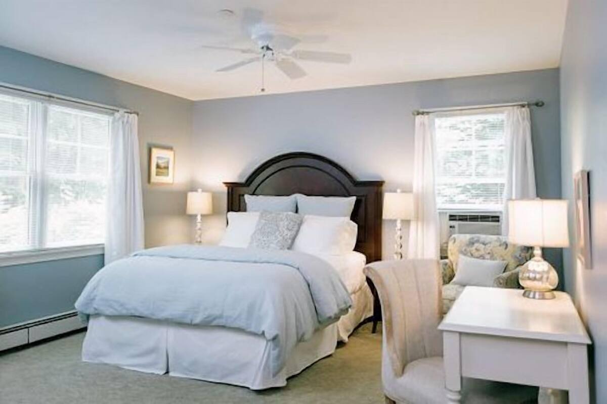 A bedroom with a bed, two bedside lamps, a ceiling fan, and a nightstand with a lamp.