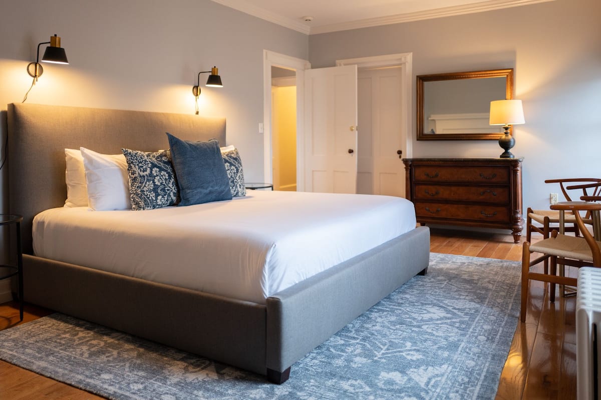 A neatly arranged bedroom with a large bed, bedside lamps, a dresser, and a chair.