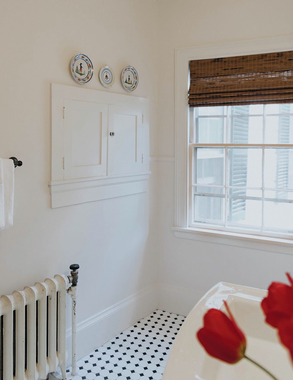 A bathroom with a white radiator, a window with blinds, and three decorative plates on the wall.
