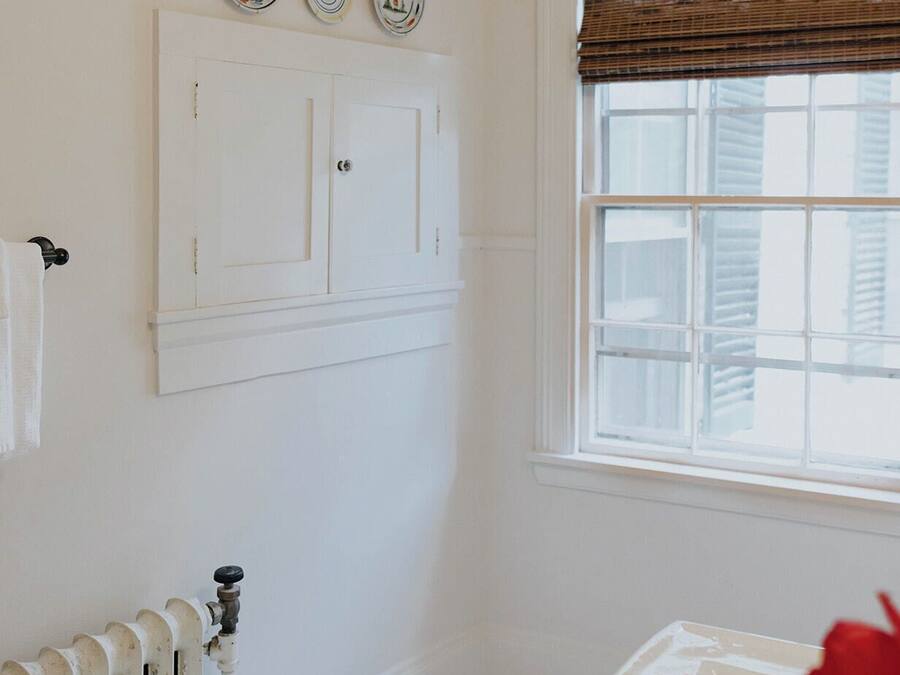 A bathroom with a white radiator, a window with blinds, and three decorative plates on the wall.