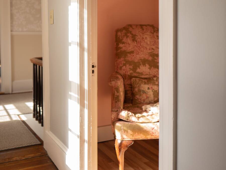 Une pièce avec un plancher en bois, un fauteuil à motifs floraux et une porte blanche.