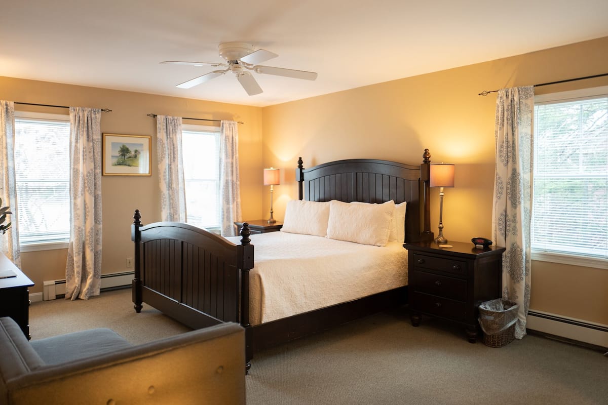 A bedroom with a bed, a nightstand, a lamp, a ceiling fan, and a window with curtains.